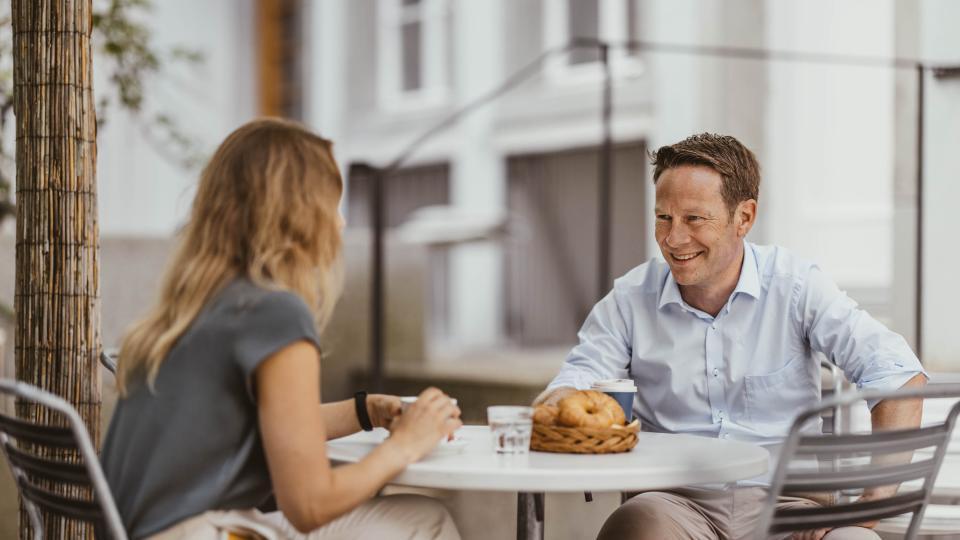 Ein paar Sitzt an einem runden weissen Tisch, trinkt Kaffee und plaudern miteinander.