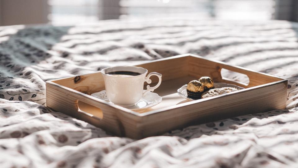 Kaffeetasse mit Schokolade steht auf einem Holztableau auf einem Bett.