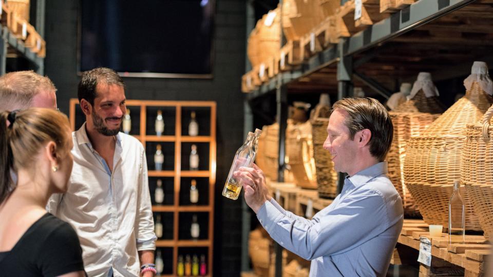 Gabriel Etter erläutert die Kunst des Brennens im Kirschkeller. Im Hintergrund stehen grosse Korbflaschen auf Regalen.