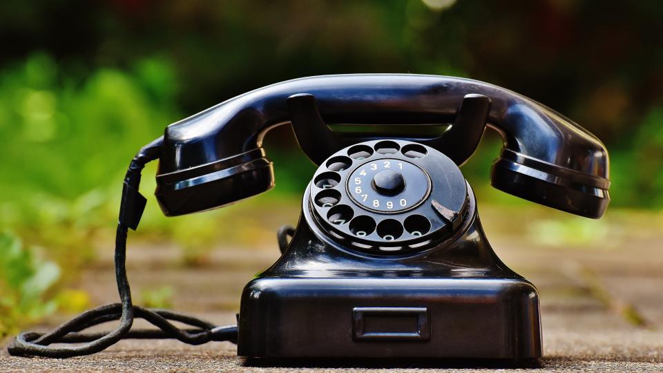 Ein altes, schwarzes Telefon mit Wählscheibe steht vor einem unscharfen, grünen Hintergrund.