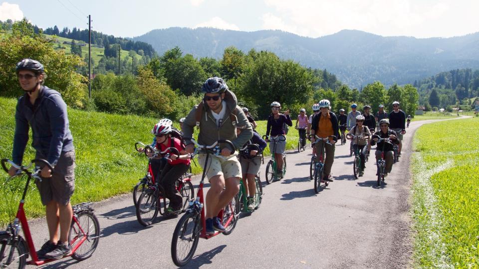 Eine Gruppe mit Trottis fährt auf einer asphaltierten Strasse.