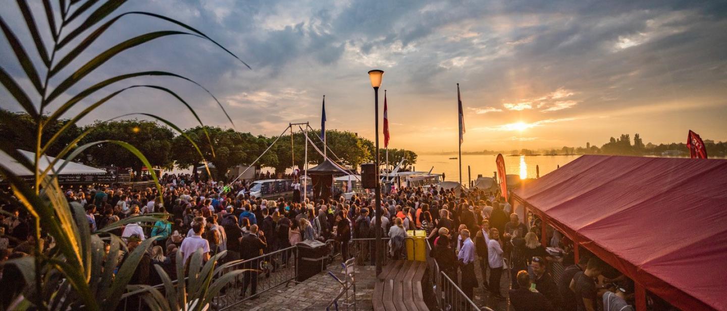 Eine grosse Masse Menschen steht am Zugersee bei Sonnenuntergang